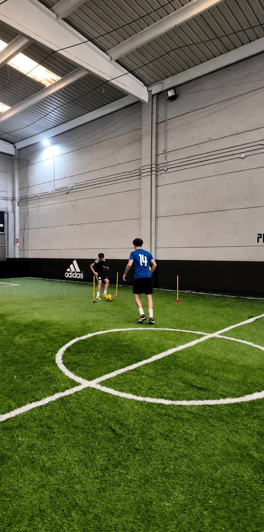 Entrenador de Premium Training Center trabajando técnica individual con un jugador en el campo de fútbol indoor en Las Rozas