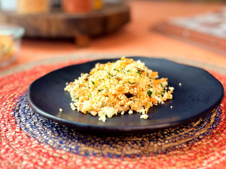 Cuscuz marroquino com sementes crocantes e ervas frescas em prato preto, sobre lugar americano de juta azul e laranja – estilo rústico.