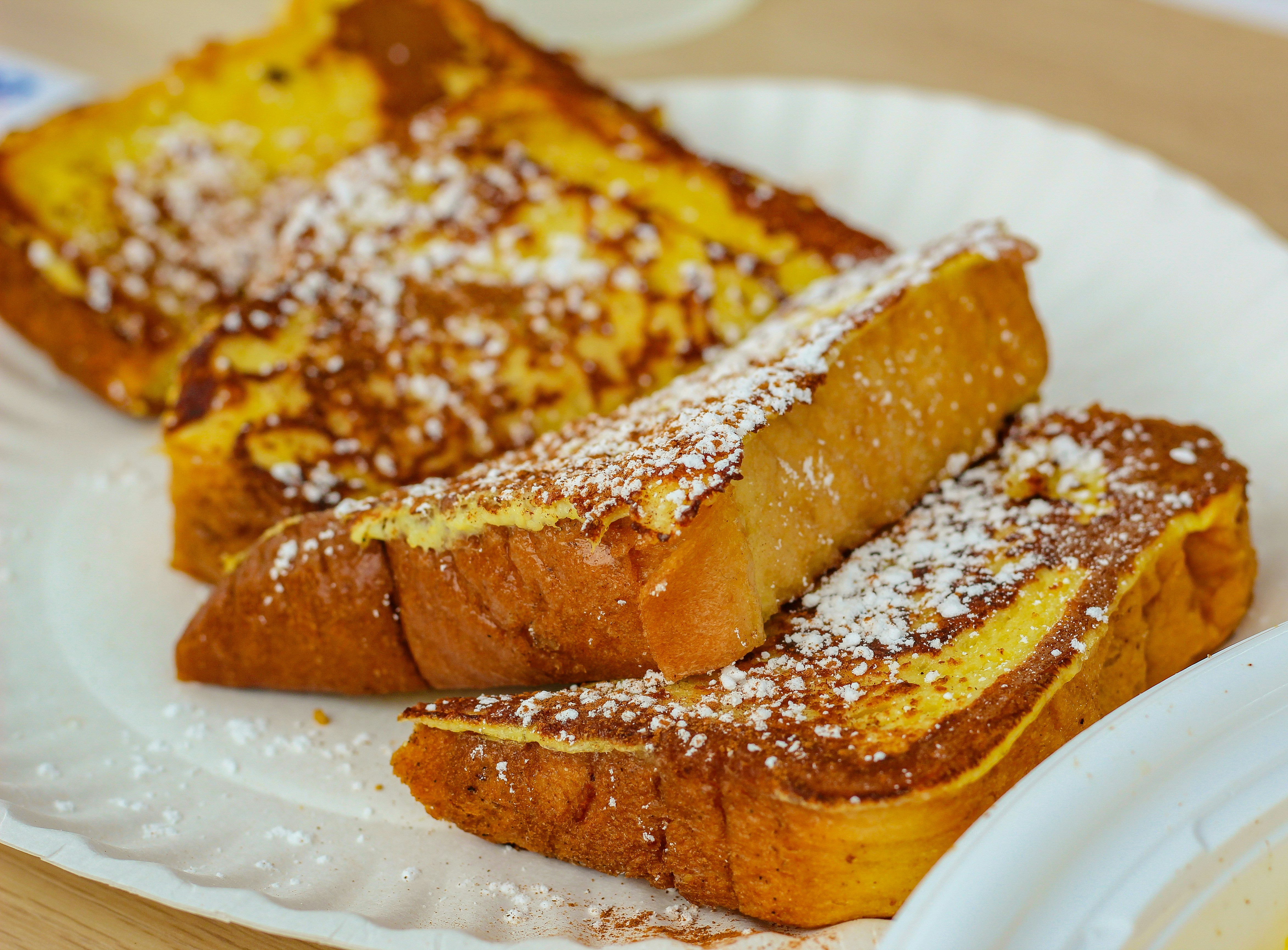 Close-up of powdered sugar-dusted French toast slices on a white plate, warm golden brown and inviting.