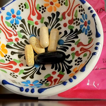 A flat-lay view of several daily vitamin capsules and tablets arranged on a clean, wooden surface next to a glass of water.