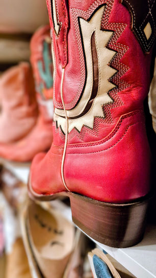 "Close-up of high-quality brown leather western boots with intricate embroidery and pointed toes, resting on a rustic wooden floor.