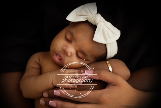 Newborn resting securely in a parent’s hands during a heartfelt session by Suzi Brown Photography
