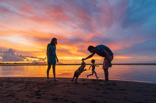 Shooting photo de famille sur la plage, au coucher du soleil, alors que le ciel de Polynésie française se colore de rouge et d'orange. Une famille qui ne se perçoit qu'en silhouettes.