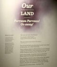 Exhibit wall with text: "Our Land, Parrawa Parrawa! Go away!" in bold. Beige background, abstract purple pattern, solemn mood.
