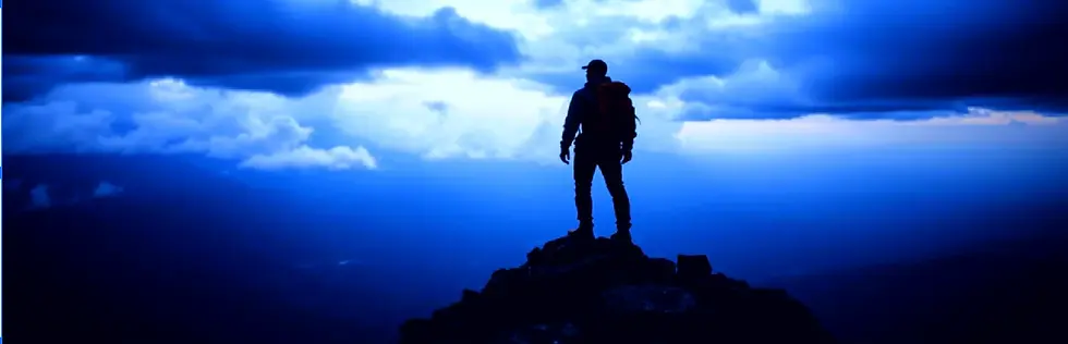 青い空と雲を背景に、山頂に立つ人のシルエット