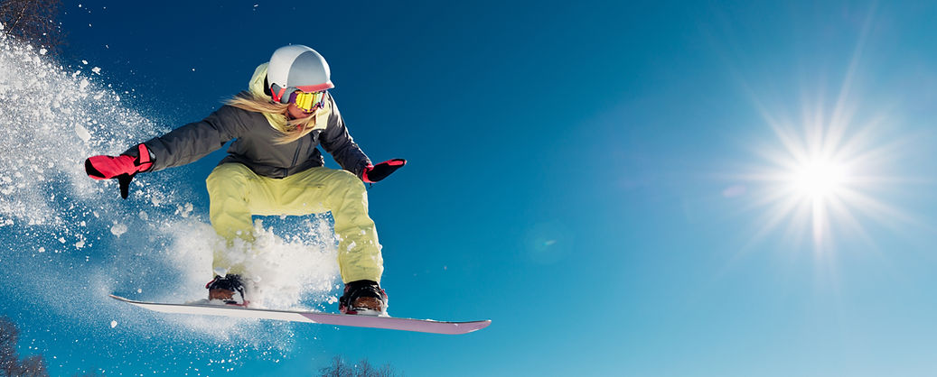 青空と輝く太陽の下、スノーボーダーが雪煙を上げてジャンプする瞬間。