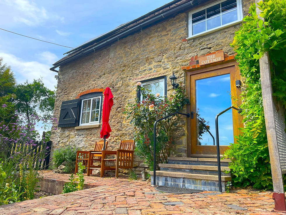 Wellspring cottage entrance at The Wellspring Ledbury with wooden door, steps, patio seating, red umbrella, and garden flowers