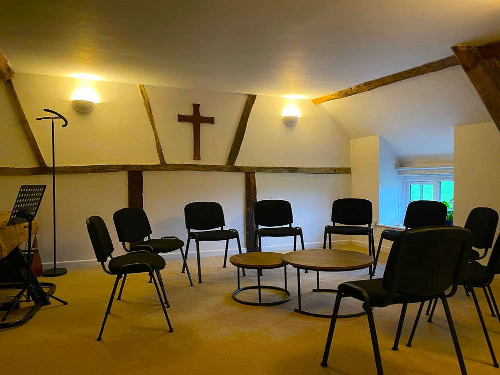 Meeting room at The Wellspring Ledbury with chairs in a circle, wooden beams, wall cross, and soft lighting