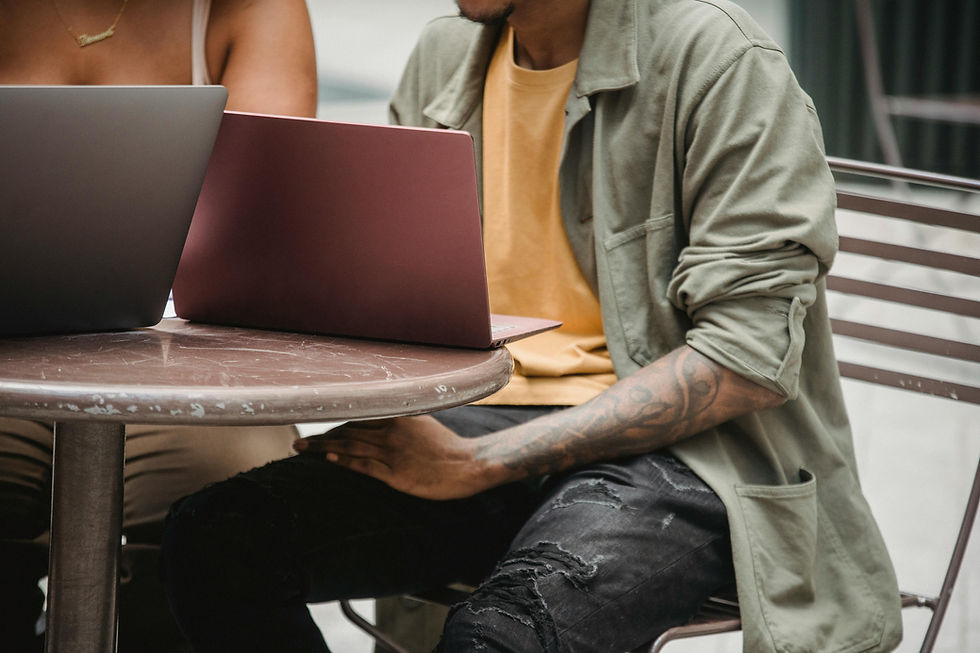 Two people sitting at an outdoor cafe table, each working on a laptop, focusing on their screens.