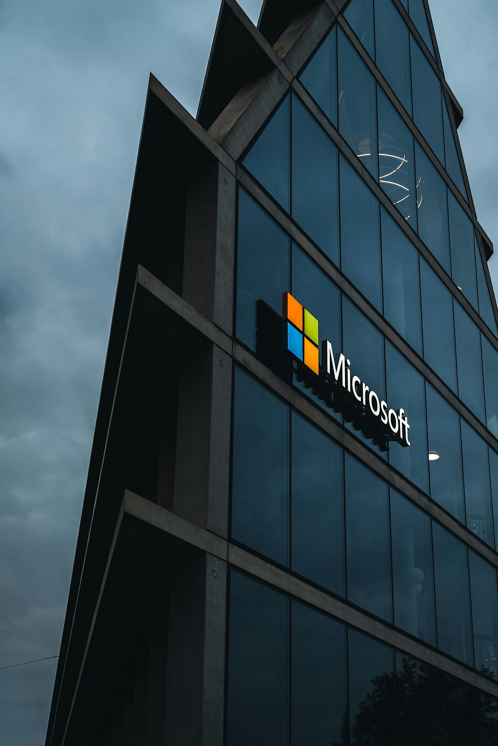 The modern facade of a Microsoft building with the company's logo prominently displayed. The image captures the corporate presence of Microsoft in an urban setting.