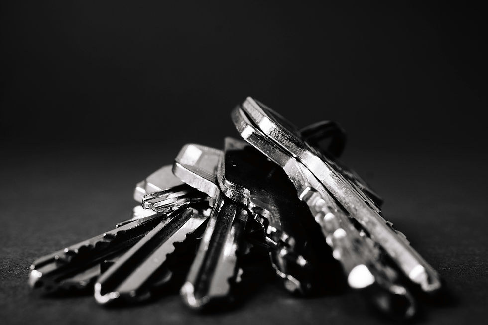 A pile of assorted keys in monochrome, focused sharply in the foreground against a blurred dark background.