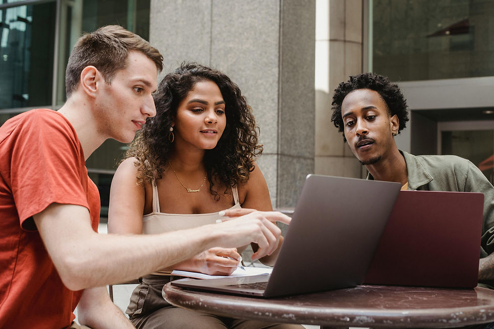 Three young professionals collaborating on a project outdoors. They are seated at a table with a laptop, engaged in discussion over their work.