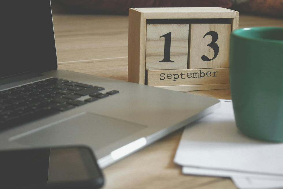 Laptop on a wooden desk with a block calendar showing September 13 and a green coffee mug.