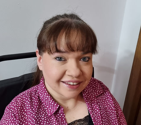 Me smiling at the camera at a slight angle and wearing a purple blouse with white spots.