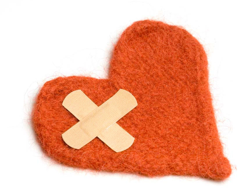 Red felt heart with a beige bandage in a cross shape on it, set against a white background. The mood suggests healing or sadness.