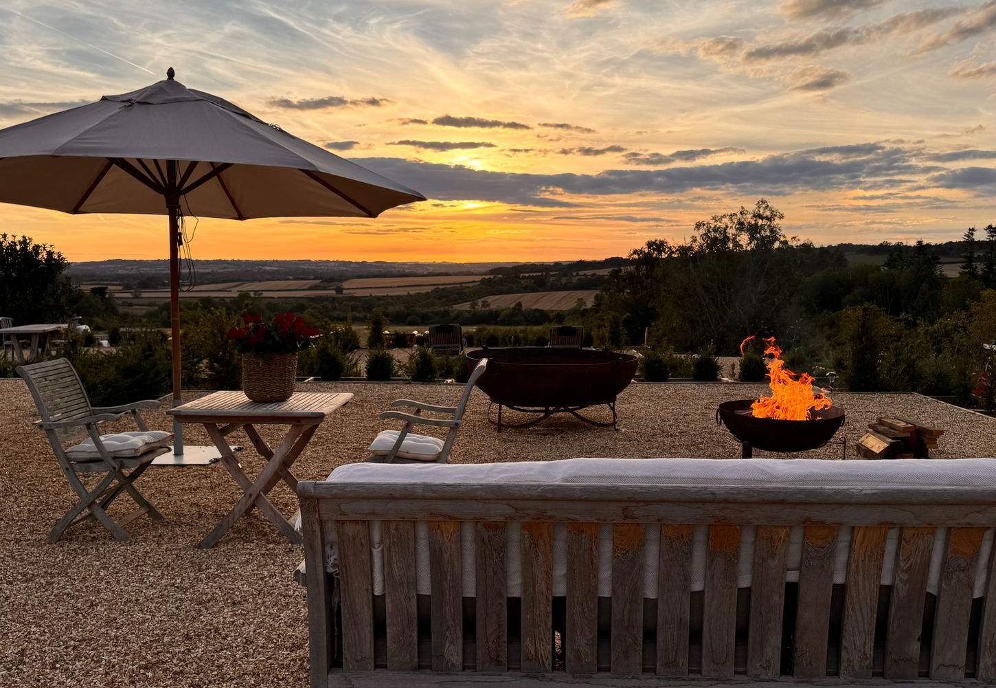 Sunset over the Cotswold countryside with a fire pit, outdoor seating, and landscaped gardens at Dovecote Cotswold Cottages.Valley. A fire-pit and parasols in view.