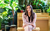 Mikayla Lanoie in a pink suit, smiling and seated in a bright room full of plants