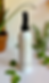 A bottle of Growth Mist Hair and Scalp Spray on a table with a white tablecloth. next to some decorative green leaves.