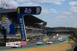 Cars driving past the starting line at Le Mans.