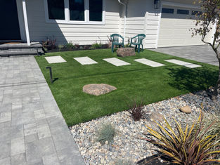Front yard synthetic turf with stone pathway, stone landscaped garden and a seating area.
