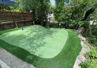 Synthetic turf putting green with four holes, curved design, and stone landscaped border.