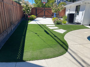 Backyard synthetic turf with stone path leading to a concrete basketball court.