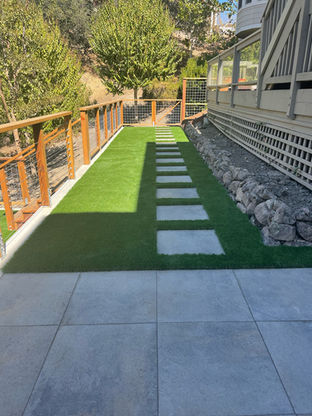 Side yard synthetic turf with stone pathway, small rock retaining wall, and fencing.