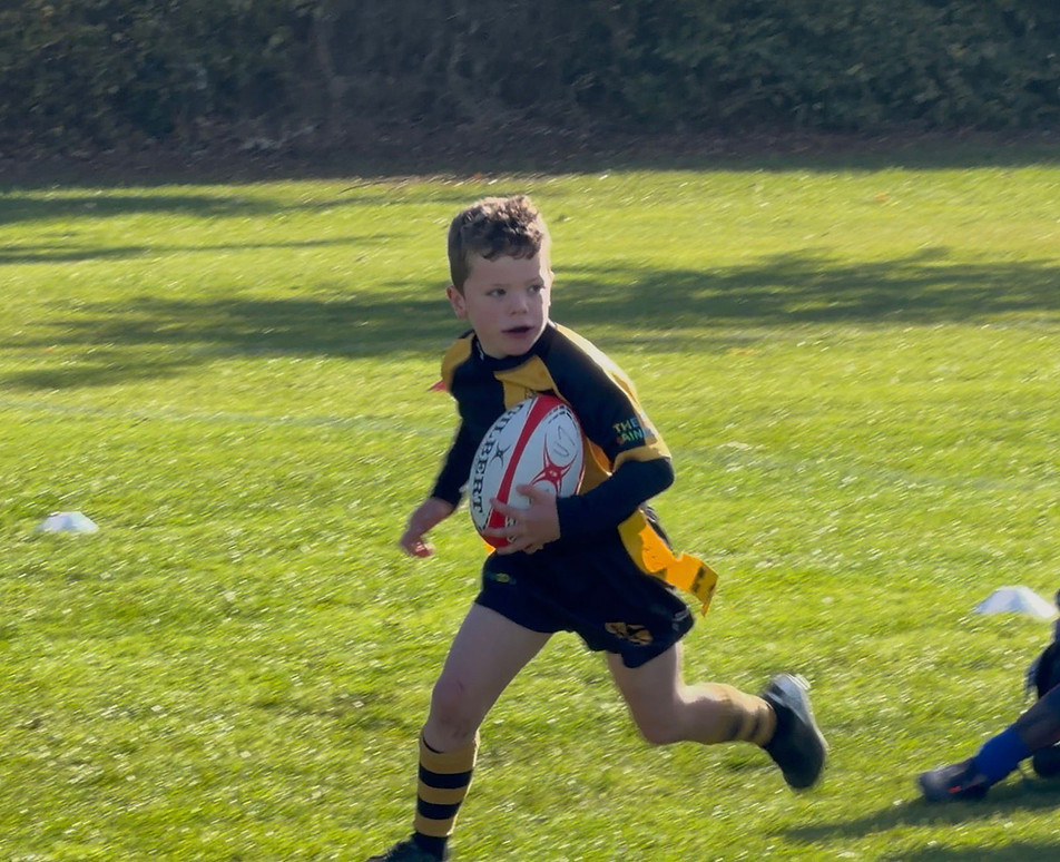 Young rugby player running with a ball on a green field.