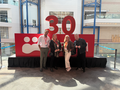 Four attendees from Priority Recruitment and Thriving Support pose for a group photo at the BABICM Conference. They are standing in front of a large red "30" display inside a bright conference venue, wearing event lanyards and badges. The image was taken during the team's attendance at the event, where they connected with professionals from across the case management, healthcare and legal sectors.