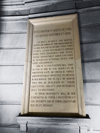Inscription of Queen Victoria’s Proclamation from November 1st, 1858, at Allahabad, carved in stone and displayed in the grand gallery of the Victoria Memorial in Kolkata. Surrounding artworks by Johann Zoffany add to the gallery’s historic ambiance, capturing significant moments of British colonial influence in India.