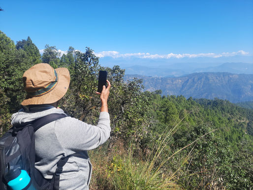 A serene winter sunset over the Himalayan foothills, with forested ridges and soft golden light.