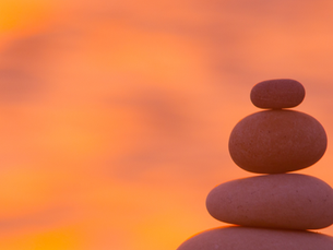 Four smooth rocks stacked on top of each other, each smaller than the one under it, with a calming sunset backdrop, representing how busy women can finish the year in peace with a year-end reflection.
