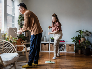 A photo of a couple cleaning and organizing the house together, each responsible for a different chore, portraying how involving other family members makes decluttering more manageable for moms.