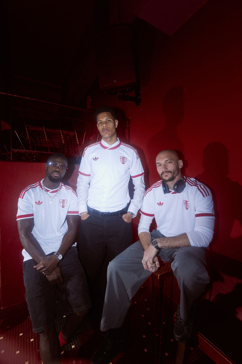 Trio posé maillot anniversaire Stade Brestois, casquette et casque audio, ambiance bar rétro — styliste Laurane Croguennec