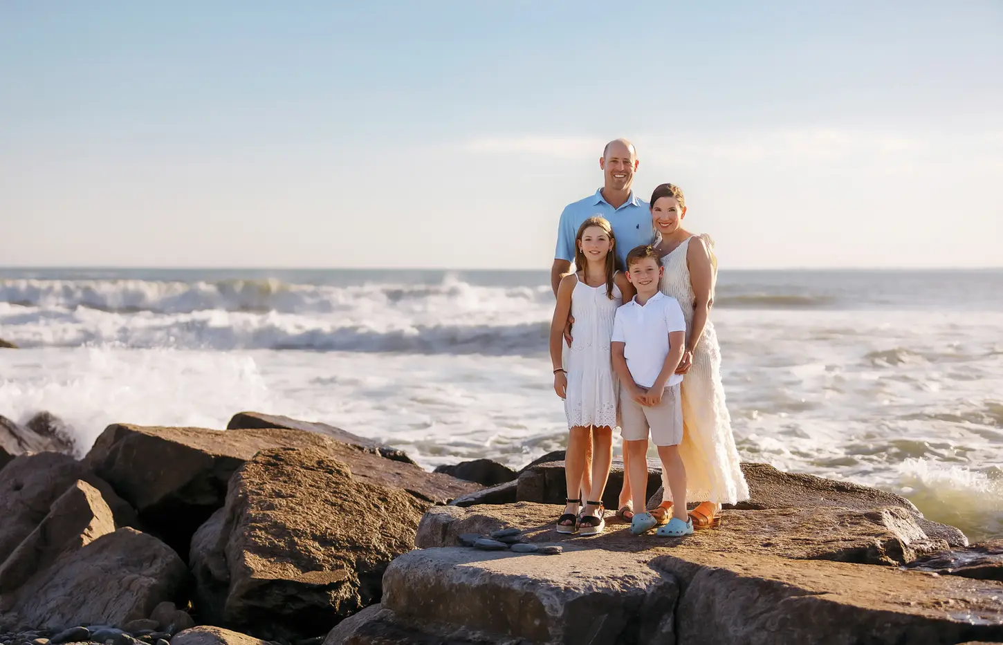 Family standing on the rocks at the beach with waves crashing behind them