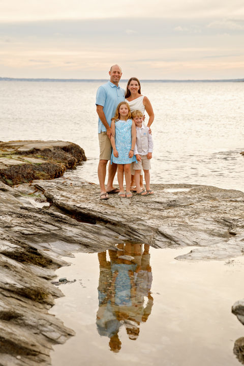 Family posing for a beautiful beach portrait during their vacation in Newport, with ocean waves in the background.