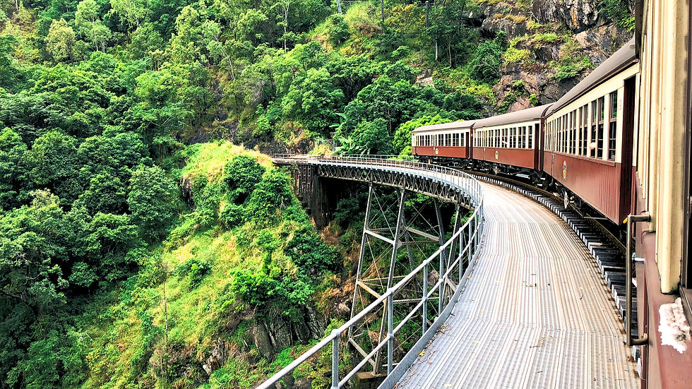 Kuranda's world-famous train curving over a high bridge through lush green mountains and rocky cliffs, seen from the carriage on a scenic route.