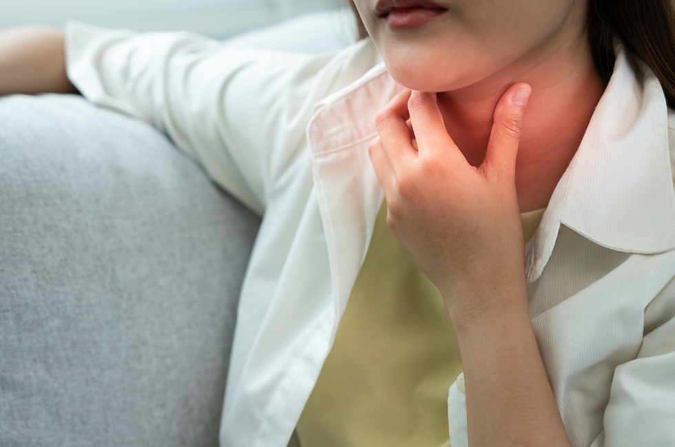 ソファでくつろぐ女性が首元を押さえ、喉の痛みや違和感を訴えるようなクローズアップ。白いシャツと淡い背景。