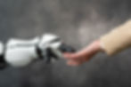 Human hand shaking a white robot hand against a gray background, symbolizing collaboration between humans and technology.