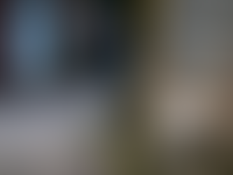 A lone kitten sitting on a curb in front of a brick wall.