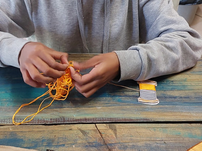A child that is busy detangling yellow thread that she was trying to roll on to a thead holder.