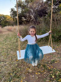 Flower girl sitting on a swing, wearing a winter flower girl outfit.