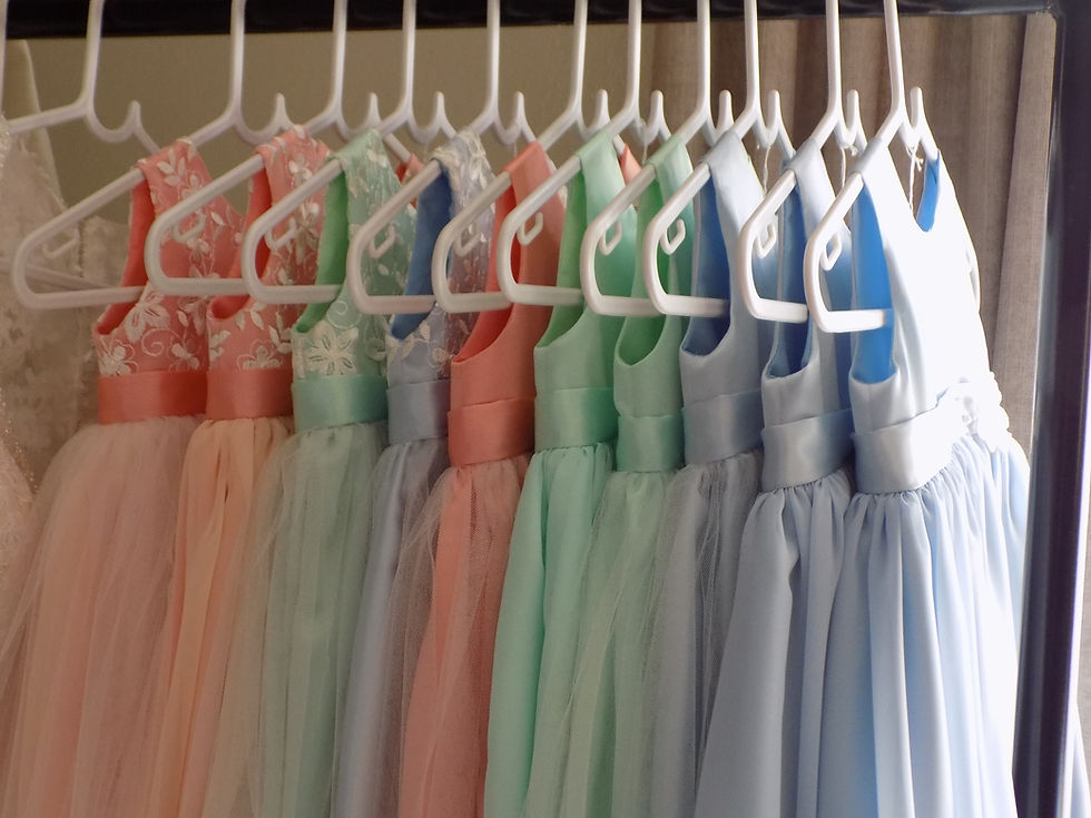 Pastel-coloured flower girl dresses are hanging on a rail in a row