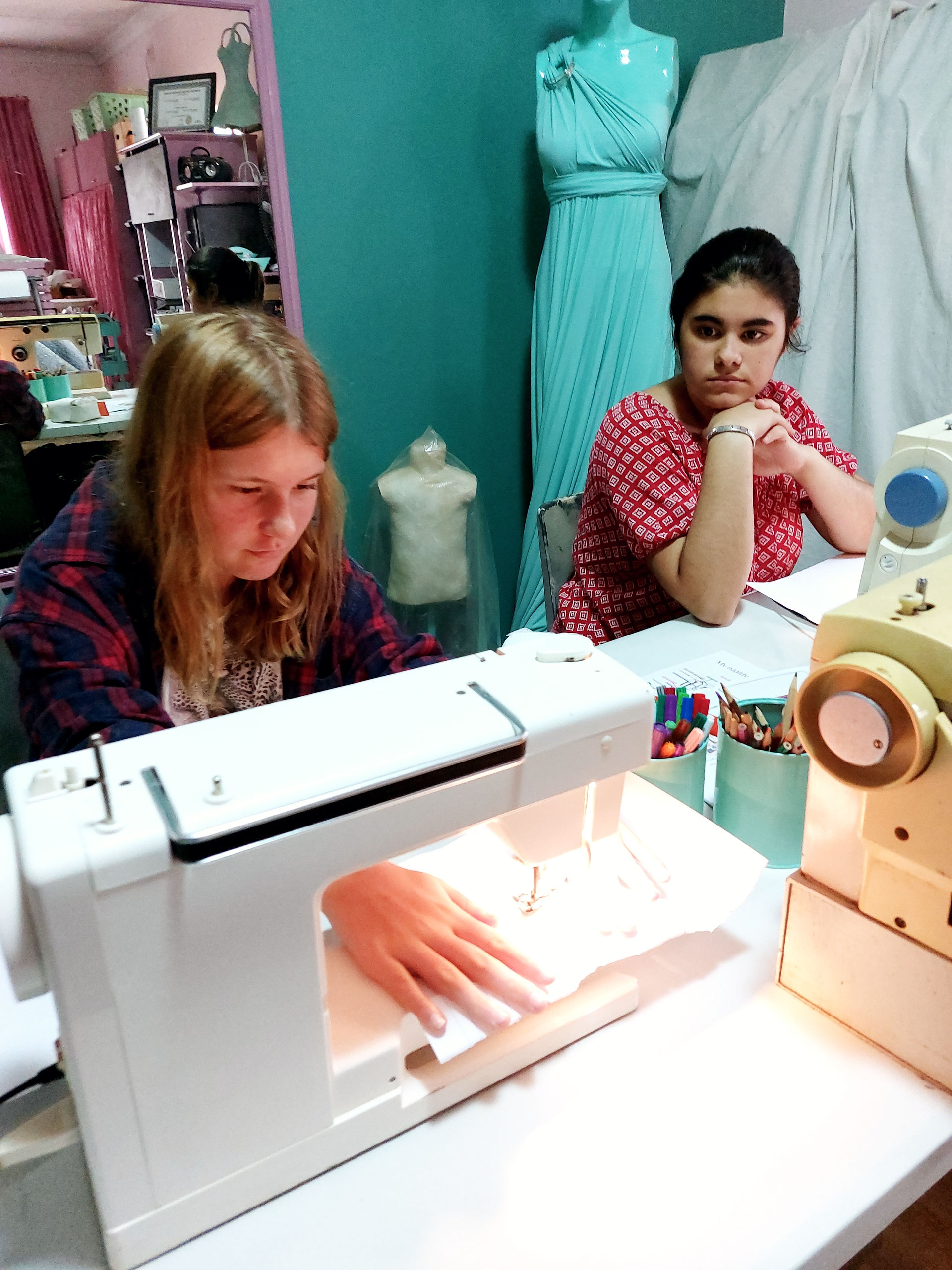 Two girls sitting behind their sewing machimes in a  sewing lesson