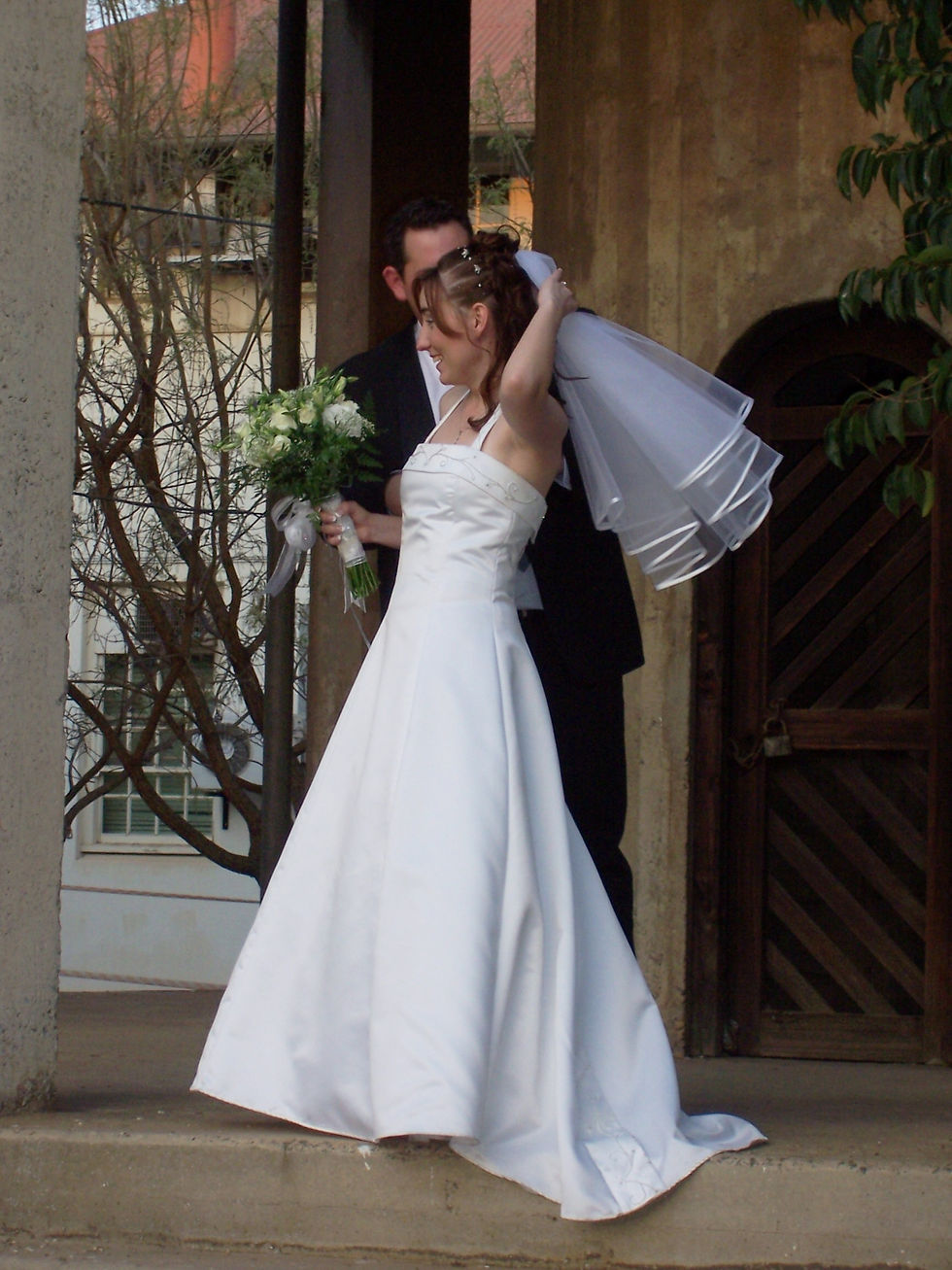 A bride in a white A-line wedding dress is standing next to the groom and holding her veil