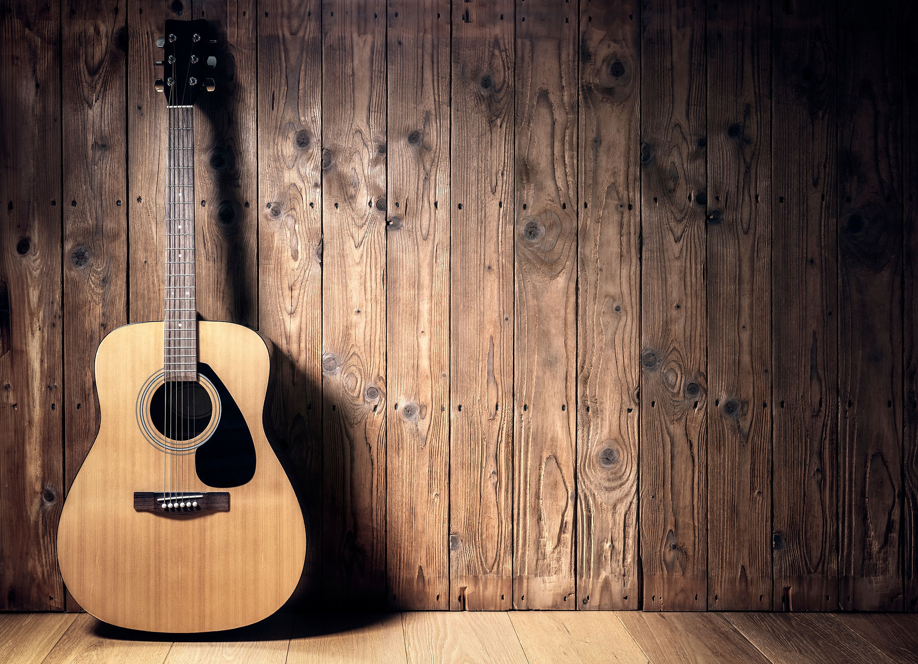 Acoustic guitar resting against a blank wooden plank grunge background with copy space.jpg
