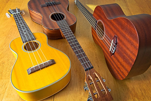 Collection of three ukuleles aligned on sun drenched wooden table top. High angle view. Si
