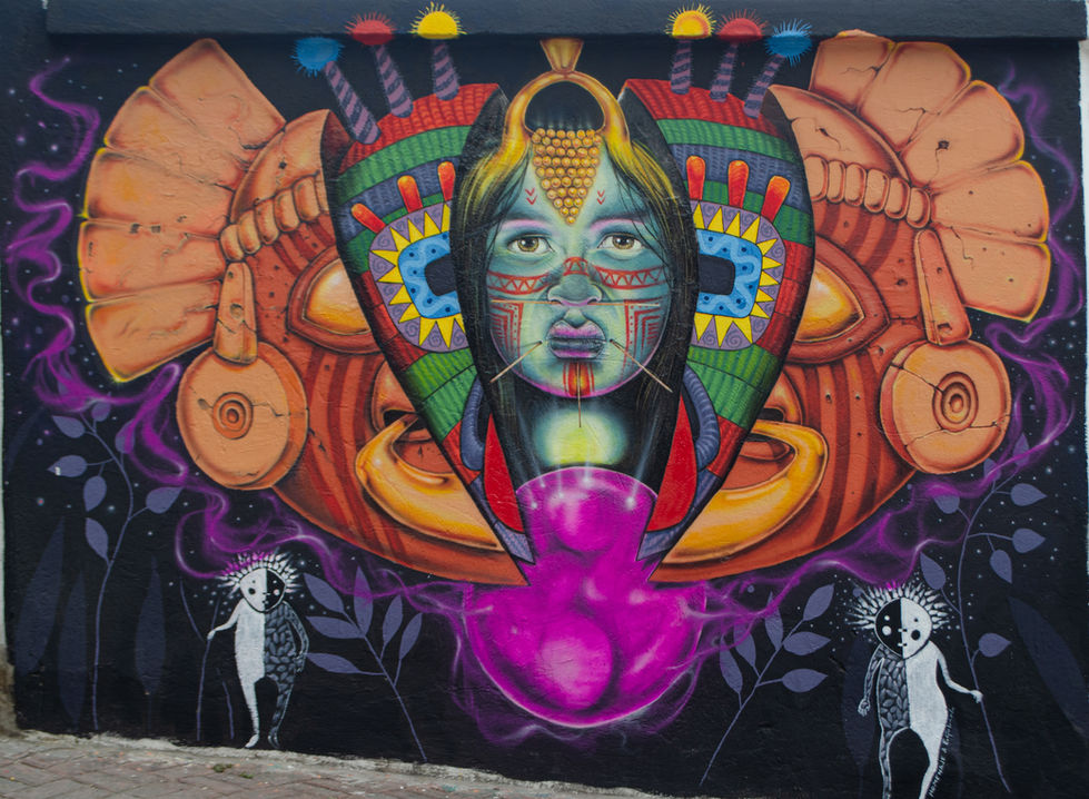 toma lateral de una intervención pictórica urbana y muralismo institucional en San Antonio de Ibarra. Se observa la perspectiva de la pared pintada en técnica de aerografía de alta gama, donde contrastan los colores minerales terracotas, amarillos y turquesas sobre un fondo negro profundo habitado por siluetas lineales etéreas.