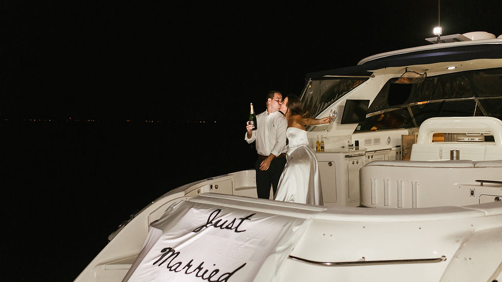 A newlywed couple shares a romantic kiss on a yacht under a starlit sky, celebrating their union with a bottle of champagne, a "Just Married" banner draped in the foreground.
