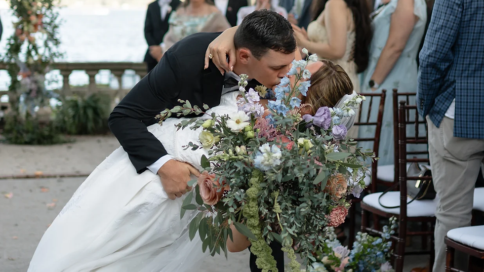 A newlywed couple shares a romantic kiss surrounded by joyful guests, with the picturesque backdrop of the Saint Johns River at The Club Continental.
